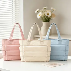 Détail de trois sacs fourre-tout matelassés en rose, crème et bleu sur une table.