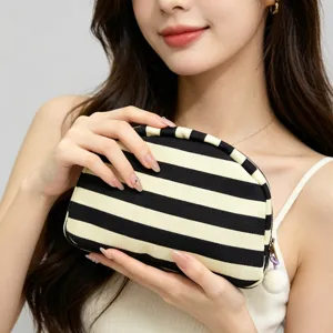 Macro detail of a striped shell-shaped makeup bag with fluffy pom-pom charm.