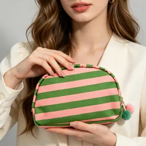 Detail view of a pink and green striped shell cosmetic bag held by a fashion model