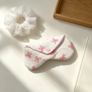 Primer plano de estuche de tela blanca para gafas con lazos rosas y botón corazón