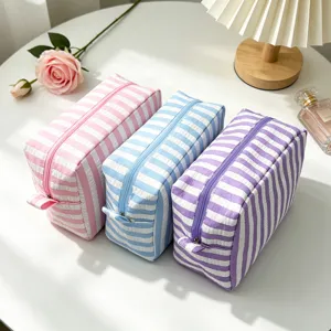 Three seersucker striped cosmetic bags in pink blue and purple displayed with rose