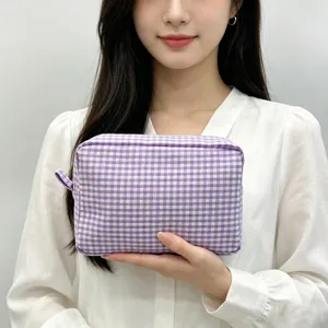 Detail view of a purple seersucker gingham cosmetic bag held by a model for scale