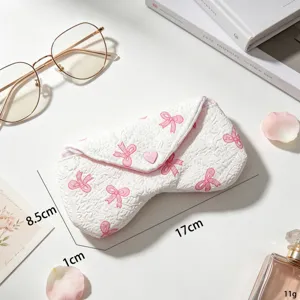 Vista detallada de una funda acolchada blanca para gafas con lazos rosas y dimensiones