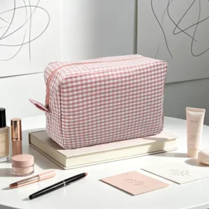 Side view of a pink gingham seersucker cosmetic bag placed on books with makeup tools