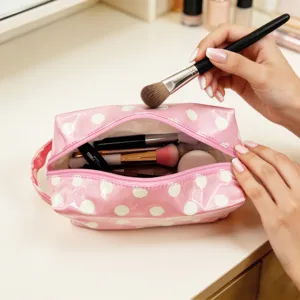 Primer plano de un neceser rosa de lunares con brochas de maquillaje en un tocador
