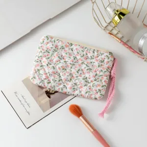 Detalle de un neceser acolchado de flores con correa rosa sobre un escritorio blanco.