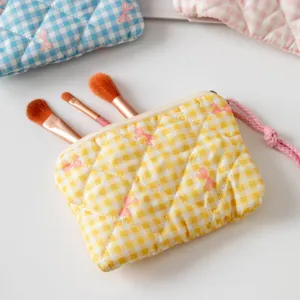 Vista detallada de una bolsa de maquillaje acolchada a cuadros amarillos con brochas