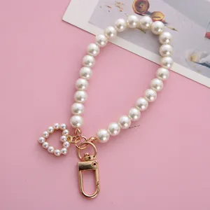 Detailed close-up of a pearl heart beaded keychain with a gold clasp on a pink aesthetic background