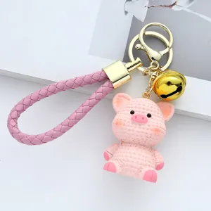 Close-up view of pink resin pig keychain with knitted texture and golden bell charm