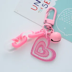 Close-up of pink heart acrylic keychain with glitter finish and bell detail.
