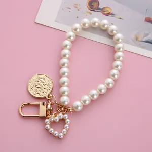 Exquisite detail of elegant white pearl keychain with golden heart and coin charm on pink background