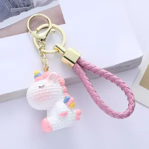 Close-up detail of a cute white resin unicorn keychain with a pink braided wrist strap.