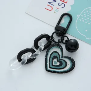 Detailed view of a glittery heart acrylic keychain with a black bell and chain.