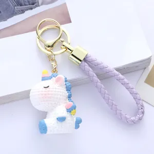 Detailed shot of a cute white resin unicorn keychain with a purple braided strap.