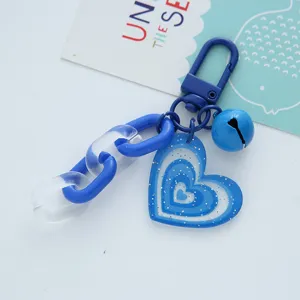 Detailed macro view of a blue heart acrylic keychain featuring glitter and a bell charm