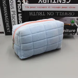 Weiche gesteppte hellblaue Kosmetiktasche mit Pfirsich-Reißverschluss auf einem Schreibtisch.