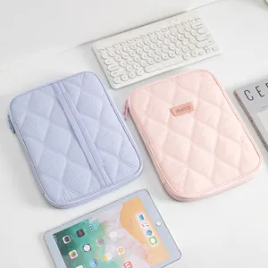 Close-up of minimalist quilted tablet sleeves in pink and purple on a clean white desk.