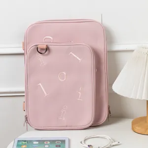 Close-up of pink embroidered laptop sleeve and iPad cross-body bag on a white desk
