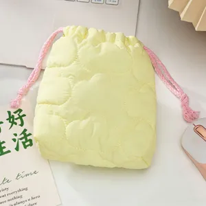 Gros plan sur la pochette matelassée jaune avec motifs nuages et cordon rose.