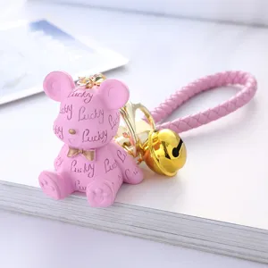 Close-up detail of a pink resin lucky bear keychain with a gold bell and braided strap