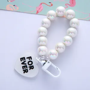 Close-up of iridescent pearl phone strap with a white heart tag featuring FOR EVER text.