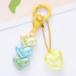 Close-up of iridescent acrylic heart pendants on a vibrant yellow metal keychain accessory