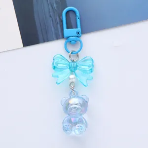 Detail view of a cute iridescent blue acrylic bear keychain with a stylish bow decoration