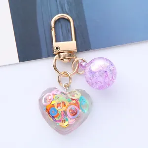 Detailed view of a heart-shaped acrylic keychain with colorful sequins and a purple ball.