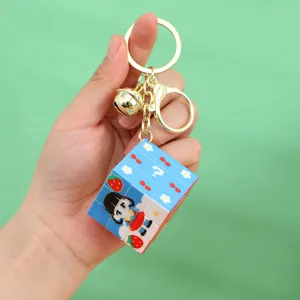 Close-up of a cartoon Rubik's cube keychain with strawberry patterns and a gold bell.