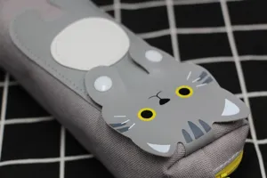 Gros plan d'une trousse à crayons en toile grise avec un appliqué chat 3D très mignon.