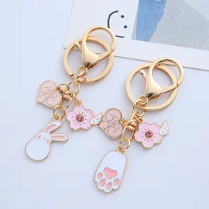 Detailed view of cute pink rabbit and cat paw enamel charms on gold metal keychain
