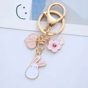 Close-up detail of pink rabbit and cherry blossom enamel charms on a golden metal keychain