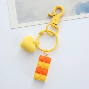 Close-up of a vibrant yellow heart and colorful brick charm keychain on a white surface.
