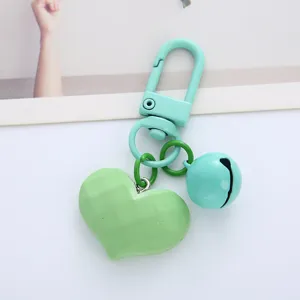 Close-up of a faceted heart charm and candy-colored bell on a mint green keychain