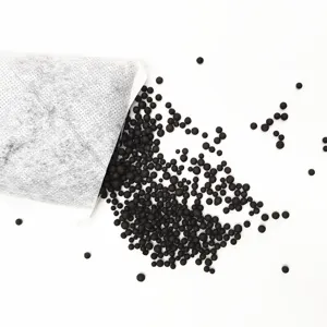 Detalle de gránulos de carbón activado negro vertiéndose de una bolsa de tela blanca.