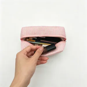 Vue détaillée d'une main mettant du rouge à lèvres dans une trousse de maquillage en seersucker