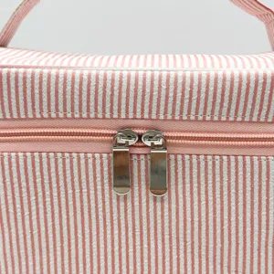 Détail d'une trousse de toilette en seersucker rayé rose et blanc avec double fermeture éclair.