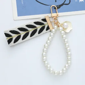 Detailed view of woven strap keychain with white pearl loop and gold shell charm.