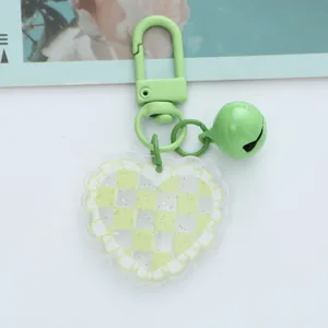 Detailed shot of a green checkerboard heart acrylic keychain with a matching bell.