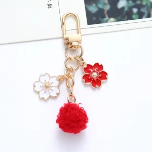 Close-up view of a Japanese style cherry blossom keychain with a soft red pom pom charm