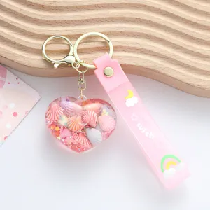 Close-up of a cute pink heart-shaped quicksand keychain with tiny shells and glitter.