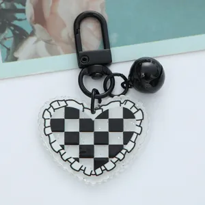 Macro detail of a heart-shaped acrylic keychain with checkered pattern and black bell.