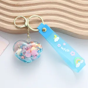 Close-up detail of a blue heart-shaped quicksand keychain with seashells and glitter