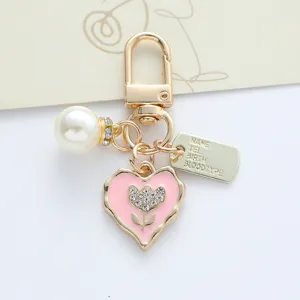 Macro close-up view of handmade heart keychain featuring pink enamel pearl and metal ID tag