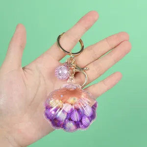 Detailed view of a purple seashell keychain with glitter quicksand effect held in hand.