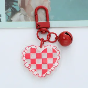 Macro view of a red checkered acrylic heart keychain with a glossy bell pendant.