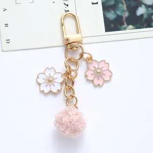 Close-up of pink cherry blossom and pom-pom keychain with gold-tone hardware