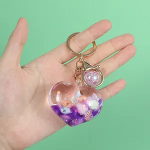 Detail view of heart-shaped liquid keychain with shells and purple quicksand glitter.