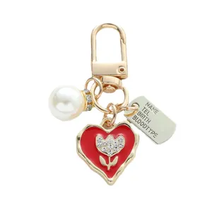 Handmade gold heart keychain featuring red enamel flower, white pearl and ID tag pendant