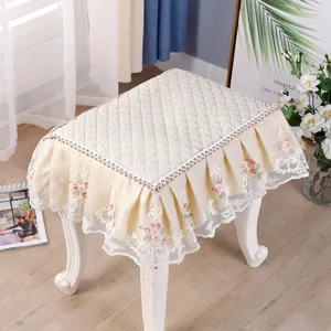 Detailed view of quilted beige square stool cover with delicate lace embroidery and ruffled trim.